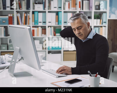 Im Büro am Schreibtisch sitzen und mit Nackenschmerzen, ist Er massierte seinen Hals: Stress und Überarbeitung Konzept Stockfoto