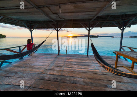 Togean Inseln Sunrise, Togian Inseln Reiseziel, Sulawesi, Indonesien. Frau beim Blick auf die Hängematte suchen, transparente türkise Wasser mit sca Stockfoto