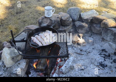 Kochen Speck in einer gusseisernen Pfanne, auf einem Grillrost, über einem heißen Lagerfeuer Stockfoto