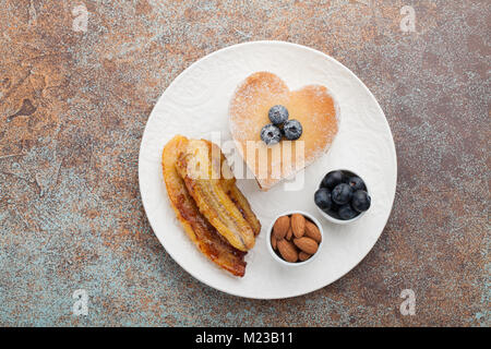 Ein Stapel von leckeren Pfannkuchen mit Honig, Kaffee und Heidelbeeren auf einem rostigen roten Hintergrund. Tolles Frühstück für den Valentinstag. Ansicht von oben mit Co Stockfoto