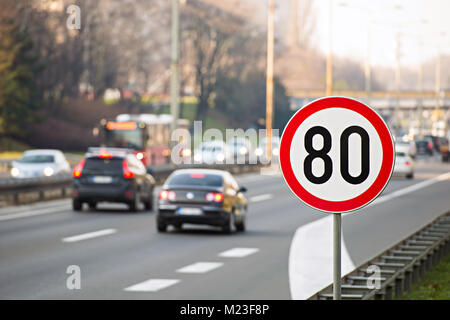 Verkehrsschild zeigt 80 km/h Höchstgeschwindigkeit auf der Autobahn voller Autos Stockfoto