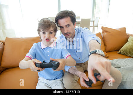 Vater und Sohn spielen Videospiel zu Hause sitzen auf der Couch Stockfoto