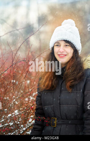 Portrait von schönen Mädchen im Winter Park an einem Strauch mit roten Beeren. Helle Lichter und Schnee. Stockfoto