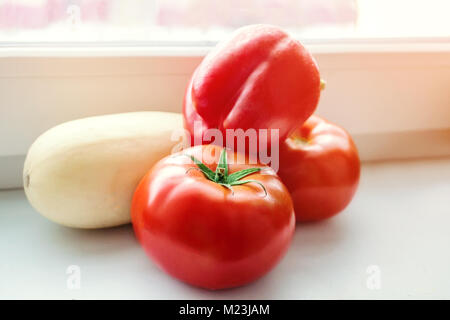 Rote reife Tomaten, Paprika und Zucchini liegen auf der Fensterbank in einem Landhaus. Farmer's Harvest. Hausgemachte Speisen. Stockfoto