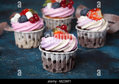 Hausgemachte Schokolade Cupcakes mit Pink Cream Cap und Beeren auf einem dunkelblauen Hintergrund. Stockfoto