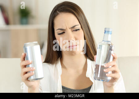 Vorderansicht Portrait von eine nachdenkliche Frau zwischen Limo trinken und Wasser zu Hause zweifeln Stockfoto