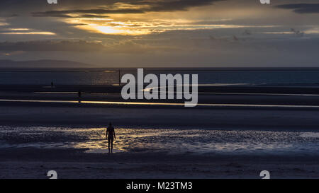 Liverpool, England, UK - 12. November 2016: Die Sonne hinter Antony Gormley' Skulpturen einen anderen Ort' auf Crosby Strand, mit den Bergen von Sno Stockfoto