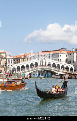 Gondoliere rudern Touristen in einer gondel vor der Rialto Brücke, Grand Canal, Venice, Veneto, Italien wie ein Wasser Taxi vorbei mit einem blauen Himmel ein Stockfoto