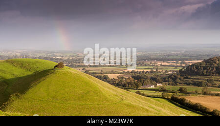 Morgen leuchtet die Landschaft der Somerset Levels und wirft einen Regenbogen an Parrock Hill, von Corton Beacon Hill im Süden von Somerset gesehen,