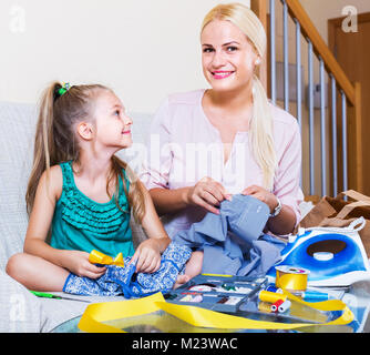 Positive Mutter Lehre kleine Tochter drinnen zu nähen. Fokus auf Mädchen Stockfoto