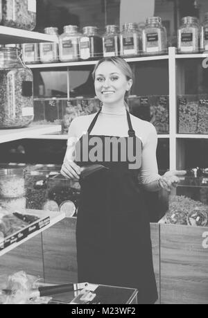 Lächelnde junge Frau mit Schürze und Verkauf von Nüssen und Trockenfrüchten in organischen Shop Stockfoto