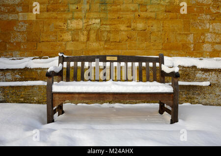 Bank unter Schnee in Tredington Kirche Friedhof oder Friedhof Warwickshire, England. Stockfoto