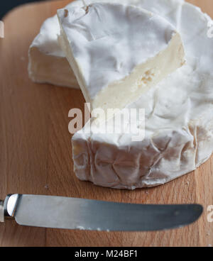 Brie Käse auf einem Holzbrett mit einem Vintage Messer. Schwarz backgeound. Makro Bild. Vertikale. Stockfoto