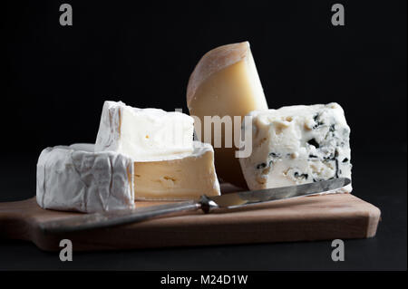 Sortiment von Käse auf einer Holzplatte mit einem Vintage Messer. Schwarzen Hintergrund. Makro Bild. Stockfoto