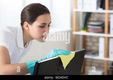 Eine junge Frau, die Reinigung der Desktop mit gelben Rag im Büro Stockfoto