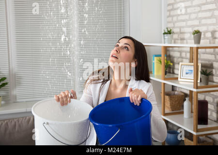 Besorgt Frau mit zwei Wannen während Wassertropfen von der Decke undicht Stockfoto