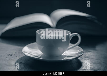 Tasse Kaffee auf dem Hintergrund der ein offenes Buch. Eine Tasse auf dem Tisch im Zimmer. Stockfoto