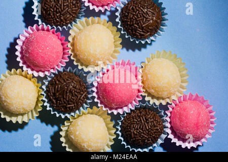 Brasilianische Spezialitäten: Brigadeiro, Beijinho und Bicho de Pe. Kindergeburtstag. Gemeinkosten der Süßigkeit, die Kugel auf blauen Tabelle. Stockfoto