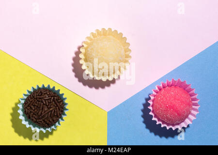 Brasilianische Spezialitäten: Brigadeiro, Beijinho und Bicho de Pe. Kindergeburtstag. Flache Ausführung von candy Kugel auf farbigen Hintergrund. Stockfoto