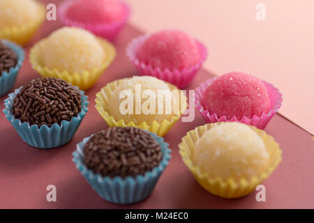 Brasilianische Spezialitäten: Brigadeiro, Beijinho und Bicho de Pe. Kindergeburtstag. Candy Kugeln in einer geraden Linie. Bunter Hintergrund. Stockfoto