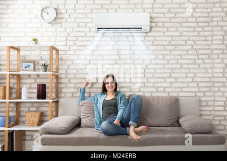 Glückliche junge Frau mit Fernbedienung Entspannen unter der Klimaanlage Stockfoto