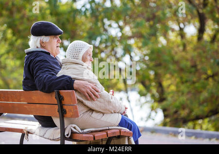 Senior Paar sitzt auf der Bank im Park und genießen Sie einen wunderschönen Herbsttag Stockfoto