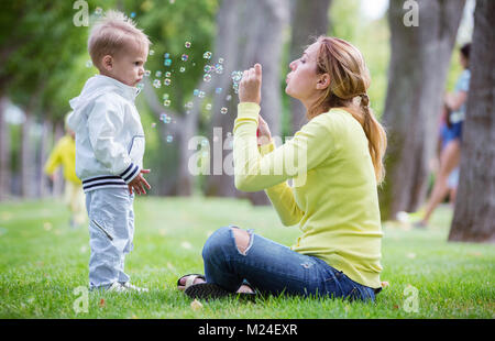 Mutter bläst Seifenblasen im Freien, kleinen Sohn beobachtete sie. Familie Spaß im Park. Stockfoto