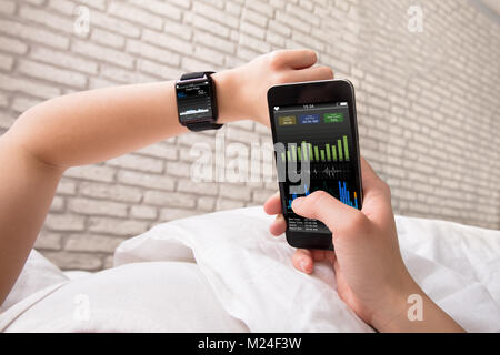 Woman's Hand zeigt Herzfrequenz auf Smart Watch und Handy Stockfoto