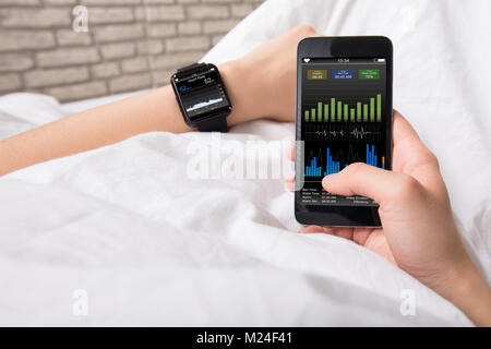 Woman's Hand zeigt Herzfrequenz auf Smart Watch und Handy Stockfoto