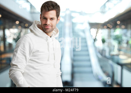 Lächelnden jungen Mann in hoodie auf Kamera und lächelnd, während vor der Rolltreppe am Einkaufszentrum. Stockfoto