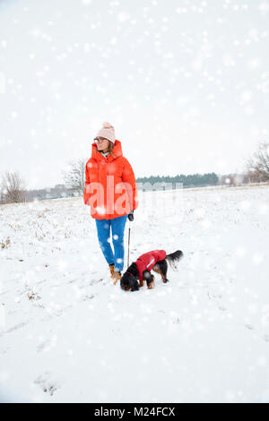 Volle Länge Schoß der Frau zu Fuß mit ihrem kleinen Hund in der Schneefall im Freien. Stockfoto