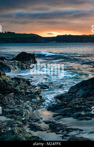 Ein Sonnenaufgang geschieht über die Felsen am Spieß Strand in St Austell, Cornwall, wie die Wellen gegen die Felsen stark strukturiert. Die Ansicht ist von S Stockfoto