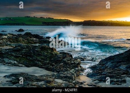 Ein Sonnenaufgang geschieht über die Felsen am Spieß Strand in St Austell, Cornwall, wie die Wellen gegen die Felsen stark strukturiert. Die Ansicht ist von S Stockfoto