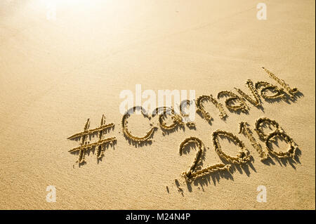 Nachricht für Karneval 2018 geschrieben auf einer glatten Sandstrand mit einer schaumigen ankommenden Welle Stockfoto