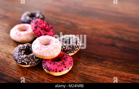 Leckere Schokolade Donuts oder frischen Krapfen mit Glasur oder Vereisung und Streuseln. Variation oder Anordnung von süßen Speisen auf einem hölzernen Tisch. das ungesunde Essen Stockfoto