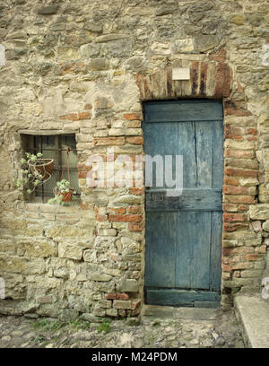 Detail einer alten Fassade mit Tür und ein kleines Fenster eines Bauernhauses Stockfoto