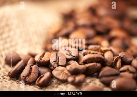 Low Angle Blick auf eine kleine Anzahl von gerösteten Kaffeebohnen auf grobem Jutegewebe in weiches Licht. Stockfoto