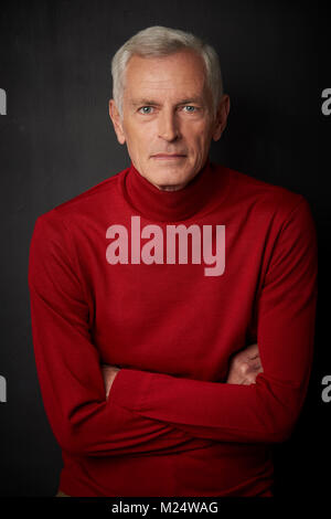Studio Portrait von Stattlichen älteren Mann mit Rollkragen Pullover und Suchen an der Kamera, während gegen bei dunklem Hintergrund stehen. Stockfoto