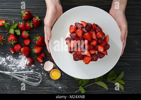 Woman's Hände, die Große platte mit Erdbeertorte, saisonbedingte Dessert kochen Stockfoto