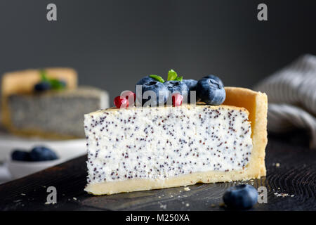 Stück Käsekuchen mit Mohn, geschmückt mit frischen Blaubeeren, Granatapfel Samen und Minze. Selektiver Fokus Stockfoto