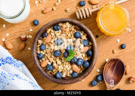 Müsli Schale mit Blaubeeren, Mandeln und Honig auf Holztisch. Ansicht von oben Stockfoto