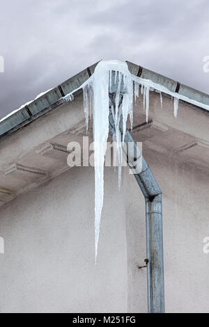 Eiszapfen hängen auf dem Dach Fallrohr entlang nach unten gegen die Wand Hintergrund Stockfoto