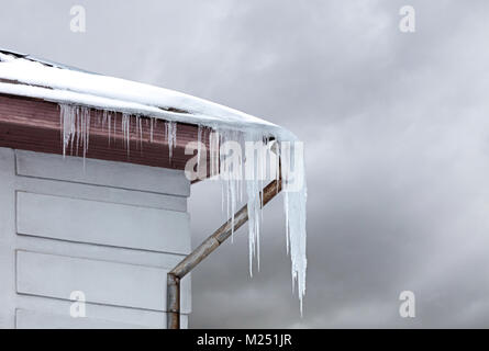 Eiszapfen hingen gefährlich vom Dach bedeckt mit Schnee Stockfoto