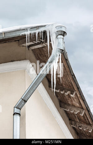 Altes haus dach mit gefährlichen großen Eiszapfen herunterhängen entlang Metall Dachrinne Stockfoto