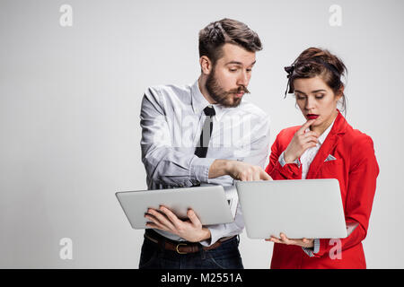 Der junge Unternehmer und Geschäftsfrau mit Notebooks kommunizieren auf grauem Hintergrund Stockfoto