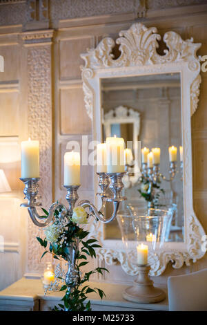 Silber Kerzenständer mit Kerzen beleuchtet und verschlungenen Blumenschmuck vor der Wand Spiegel Stockfoto