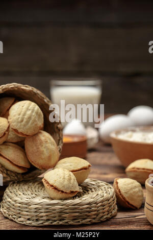 Köstliche Walnuß-förmige Mürbeteiggebäck sandwich Cookies mit süße Kondensmilch gefüllt und gehackten Pistazien auf braun Ton teller. auf alten Holz- Hintergrund, Ansicht von oben, close-up Stockfoto