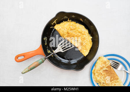 Omelette mit geschmolzenem Käse in einer Pfanne auf einem hellen Hintergrund Stockfoto