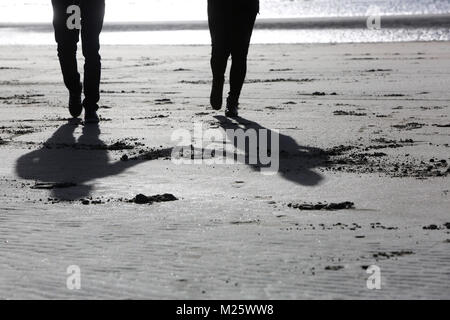 Ein paar dargestellt halten sich an den Händen und laufen am Strand entlang in West Wittering, West Sussex, UK. Stockfoto