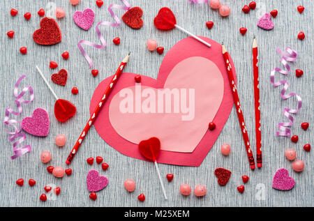 Handmade Valentinstag Karte mit roten Stifte, rot und rosa Bonbons, funkeln Herzen und gewellte Bänder auf Grau strukturierten Hintergrund Stockfoto